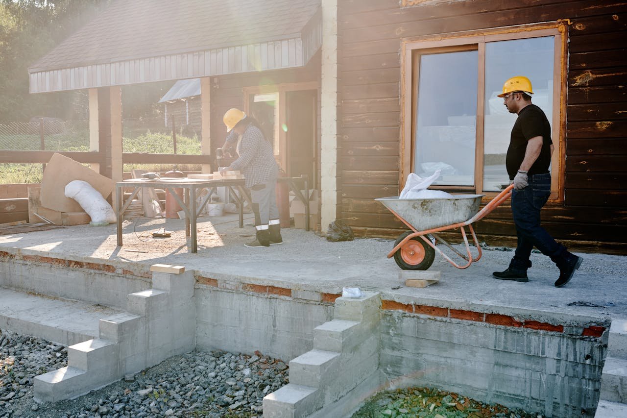 Two construction workers renovating a house exterior, carrying materials and working on woodwork.